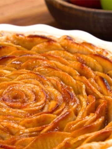 close up of apple rose pie with apples in background.
