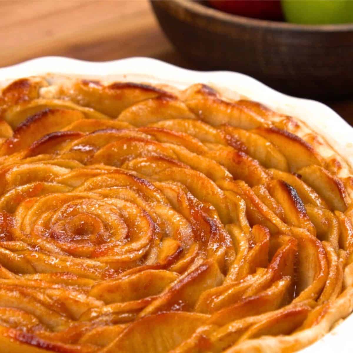 close up of apple rose pie with apples in background.