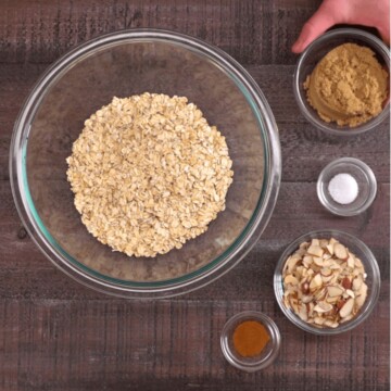 Ingredients of baked oatmeal on board including oats, cinnamon, sliced almonds, brown sugar, and salt.