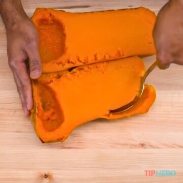 Scooping out the pulp of the butternut squash on cutting board.