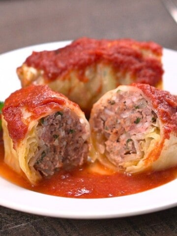 Two cabbage rolls on white plate. One cabbage is cut in half in foreground.