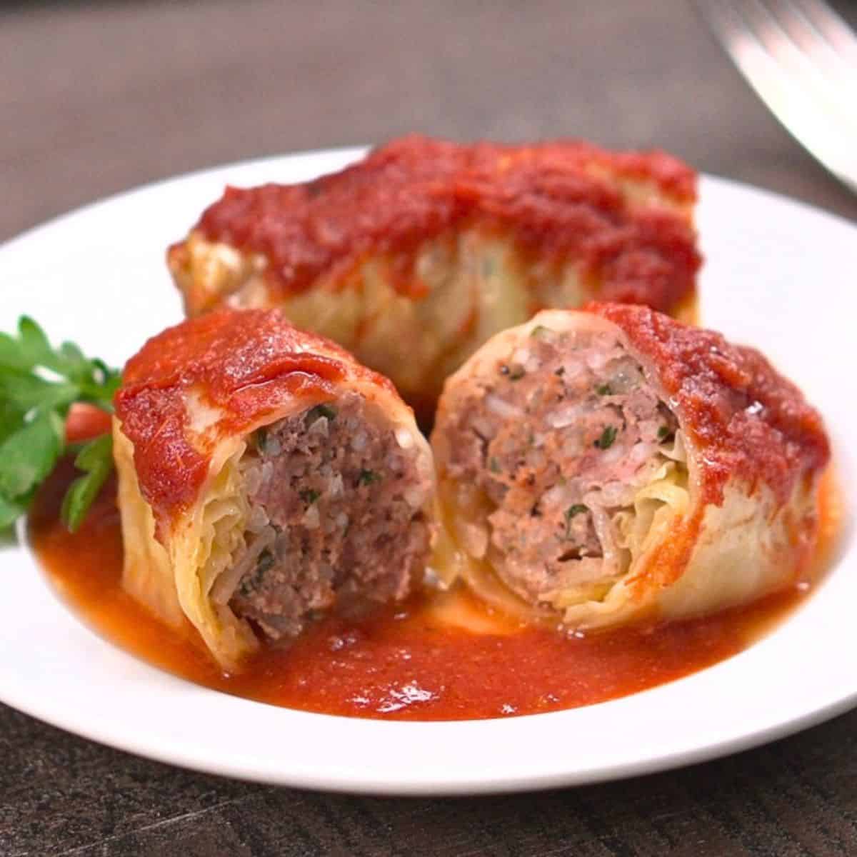Two cabbage rolls on white plate. One cabbage is cut in half in foreground.