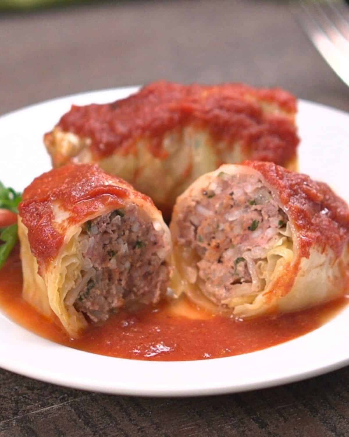 Two cabbage rolls on white place in sauce. Front cabbage roll is cut in half.