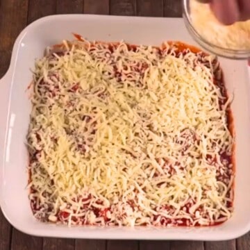 Pouring cheese on top of chicken parmesan casserole.