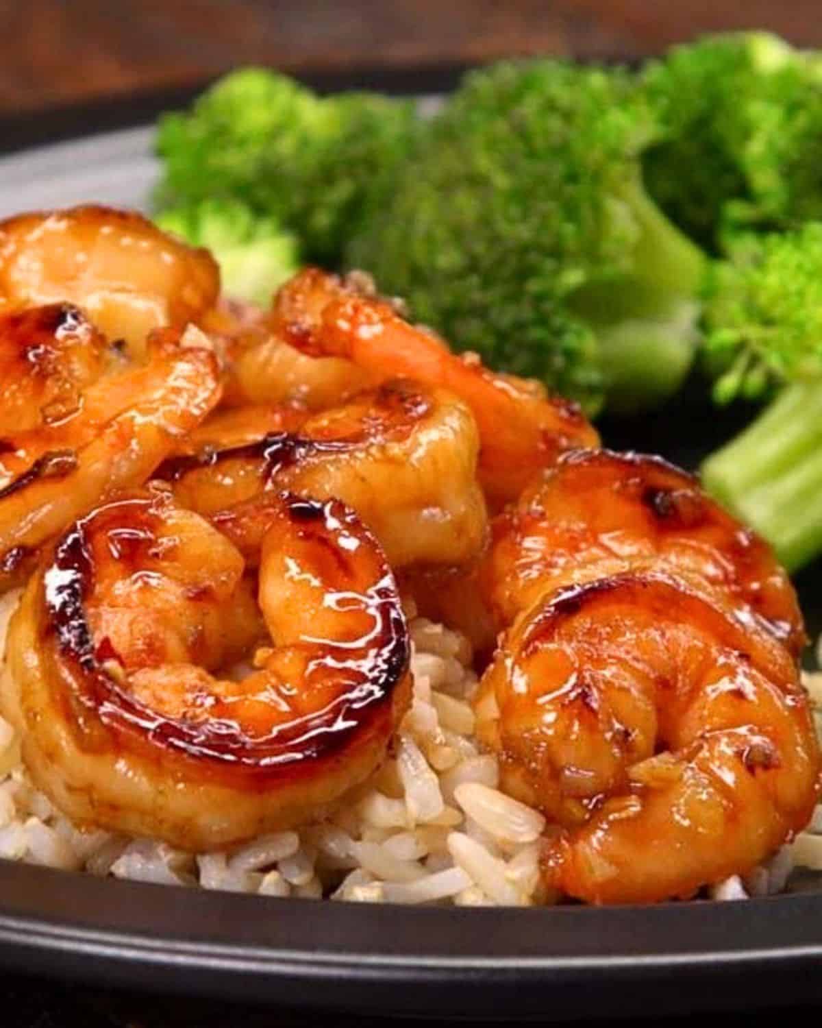 honey garlic shrimp on black plate with rice and broccoli.