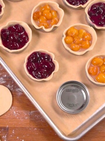 Fruit pie filling in mason jar lids on baking sheet.