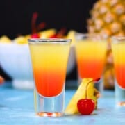 Pineapple Upside Down Cake Shots with pineapple and bowl of cherries.