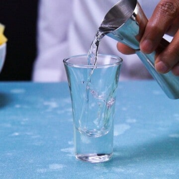 Pouring vodka into shot glass with jigger.